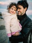 Cena fofa de pai segurando e abraçando sua filhinha na praia no inverno — Fotografia de Stock