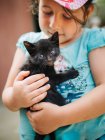 Zarte Szene eines süßen kleinen Mädchens, das eine kleine schwarze Pussycat hält und schaukelt — Stockfoto