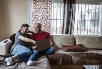 Joyeux couple gay en utilisant un ordinateur portable tout en se relaxant sur le canapé — Photo de stock
