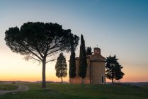 Тихий ландшафт малої каплиці з деревами в дистанційному зеленому полі на заході сонця в Тоскані, Італія — стокове фото