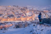 Visão traseira do viajante admirando a vista pitoresca da cidade nevada iluminada contra o fundo do céu crepúsculo — Fotografia de Stock