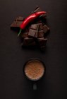 Pieces of yummy chocolate placed near black mug of steamy hot beverage with chili pepper on dark background — Stock Photo