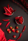 Tecido vermelho e galhos com botões brilhantes colocados no fundo preto perto de pimentas quentes e morangos maduros doces — Fotografia de Stock