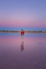 Femme prenant des photos avec caméra dans un ciel bleu rose sur le bord de mer calme vide — Photo de stock