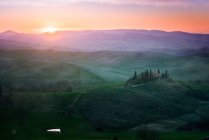 Paysage pittoresque de champs verdoyants avec chalet et arbres dans la lumière du coucher du soleil, Italie — Photo de stock