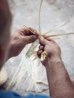 Manos de artesano anónimo usando gancho para tejer fibras secas de hojas de palma mientras trabaja en el taller - foto de stock