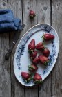 Plate of delicious ripe strawberries on wooden tabletop near blue napkin and metal knife — Stock Photo