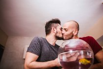 Affectionate gay couple kissing in front of aquarium with fish — Stock Photo
