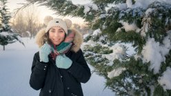 Молодая привлекательная женщина в теплой одежде с мехом радостный смех рядом с покрытым снегом хвойных деревьев — стоковое фото