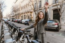 Elegante joven dama eligiendo alquiler de bicicletas en el estacionamiento y señalando con el dedo - foto de stock