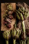 Alcachofas frescas maduras con servilleta sobre mesa de madera marrón - foto de stock