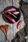 Fresh ripe eggplants on plate with chilli pepper on weathered wooden tabletop — Stock Photo