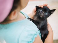 Tenera scena di carina bambina con in mano e dondolo una piccola gattina nera — Foto stock