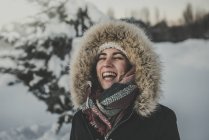 Joven atractiva hembra en ropa de abrigo con piel alegre riendo junto a un árbol cubierto de coníferas de nieve - foto de stock