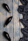 Frische reife Auberginen in der Nähe von gestreiftem Tuch auf verwitterter Holztischplatte verstreut — Stockfoto