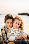 Веселий і милий хлопчик і дівчинка посміхаються і обіймають один одного на пляжі — стокове фото