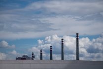Impilamenti industriali di scarico in fila dietro parete grigia su sfondo di cielo pittoresco nuvoloso — Foto stock