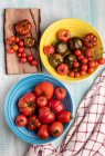 Holztisch mit Schalen mit verschiedenen frischen roten Tomaten — Stockfoto