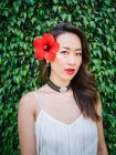 Portrait of a young classy chinese woman against leaves background with red flower in head — Stock Photo