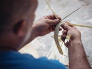 Hände eines anonymen Handwerkers mit Haken zum Weben getrockneter Palmblätterfasern während der Arbeit in der Werkstatt — Stockfoto