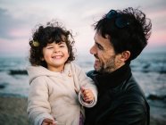 Linda escena de papá sosteniendo y abrazando a su hija pequeña en la playa en invierno - foto de stock