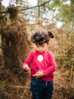 Portrait de mignonne petite fille en pull rouge debout au milieu de la forêt — Photo de stock