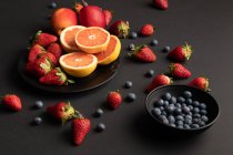 Verschiedene frische Früchte und Beeren auf schwarzem Hintergrund verstreut — Stockfoto