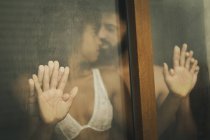 Bello ispanico ragazzo toccare e baciare seducente donna afroamericana in reggiseno di pizzo mentre in piedi dietro la finestra bagnata — Foto stock