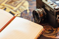 Close-up de notebook aberto ao lado de uma câmera vintage na mesa decorativa — Fotografia de Stock