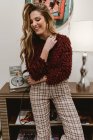 Lächelnde junge Frau im trendigen Outfit lehnt auf Schrank in stilvollem Raum — Stockfoto