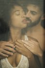 Handsome Hispanic guy touching and kissing seductive African American woman in lace bra while standing behind wet window — Stock Photo