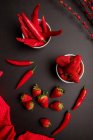 Tessuto rosso e ramoscelli con boccioli luminosi disposti su fondo nero vicino peperoncini piccanti e fragole dolci mature — Foto stock