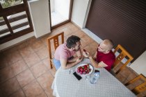 Alegre gay casal comer morangos no mesa no cozinha — Fotografia de Stock