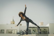 Красивая афроамериканка в стильном наряде, балансирующая на стене против безоблачного неба — стоковое фото
