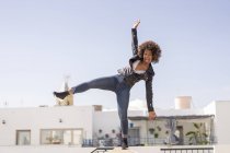 Hübsche Afroamerikanerin balanciert in stylischem Outfit auf Hauswand gegen wolkenlosen Himmel — Stockfoto