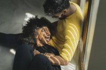 Piuttosto allegra donna afroamericana ridendo mentre giace sulle ginocchia di uomo barbuto sul pavimento — Foto stock