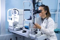 Trabajadora médica joven que usa microscopio en el lugar de trabajo con fondo borroso - foto de stock