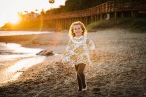Nettes kleines Mädchen in Kleid, das an der Strandpromenade unter einem wunderschönen Sonnenuntergang spaziert — Stockfoto