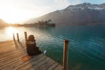 Vue arrière de la femme assise sur une jetée en bois au-dessus d'un lac turquoise dans les montagnes enneigées de Suisse — Photo de stock