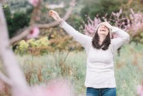 Excited female in sweater and hat standing in amazing spring countryside with blooming trees — Stock Photo