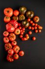 Tomate maduro fresco sortido espalhado na superfície preta — Fotografia de Stock