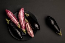 Set frischer reifer Auberginen auf Teller auf schwarzem Tisch — Stockfoto