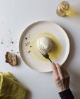 Hand of anonymous person holding fork over piece of yummy fresh burrata on plate near bread and oil against white background — Stock Photo