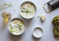 Bols de délicieuse soupe à la crème d'asperges avec du fromage et des herbes sur fond blanc — Photo de stock