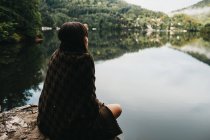 Woman sitting with blanket near lake and mountains — Stock Photo