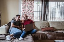 Alegre gay pareja usando laptop mientras relajante en sofá - foto de stock