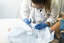 Doctora en uniforme y máscara médica sacando puntos de sutura del paciente en servilleta - foto de stock