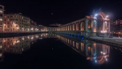 Extérieur des bâtiments modernes et pont traversant l'eau calme de la rivière illuminé dans la nuit, Suisse — Photo de stock