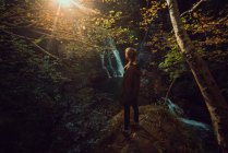 Vue arrière d'une femme dans une petite rivière et une cascade coulant dans une forêt verte sombre et belle. — Photo de stock