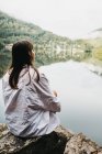 Woman sitting on rock near lake and mountains — Stock Photo